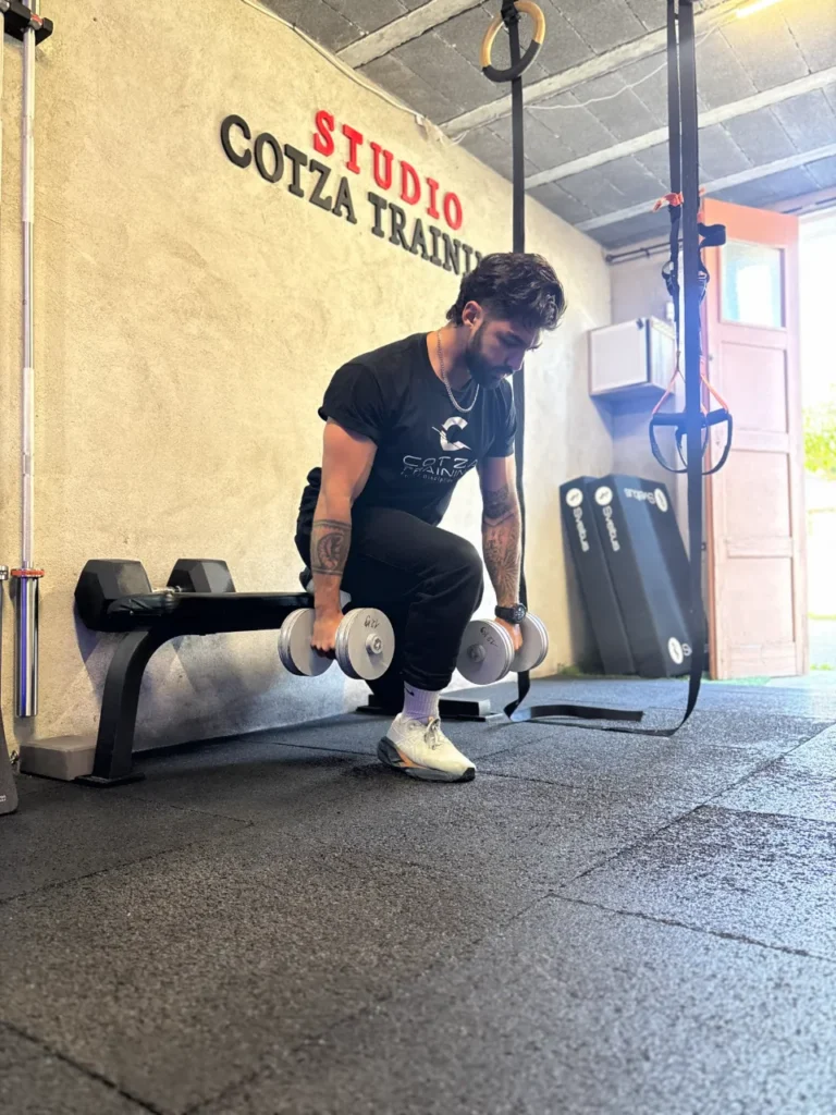 Un homme aux tatouages effectue un exercice de musculation avec haltères dans un studio de fitness.