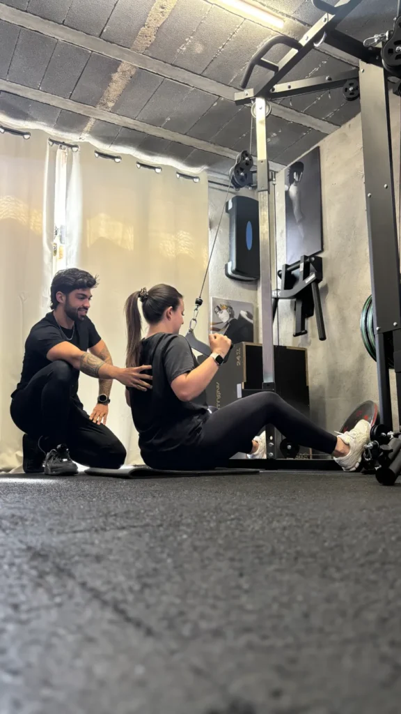 Un coach supervise une femme effectuant un exercice de tirage avec une machine à poulie dans une salle de sport.